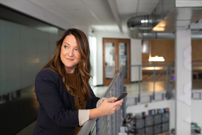 Woman in a blazer smiling at a message on her phone